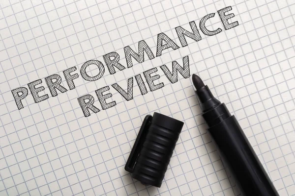 Words Performance Review and open black marker on checkered paper upper view. Labor productivity and efficiency concept. Employee evaluation