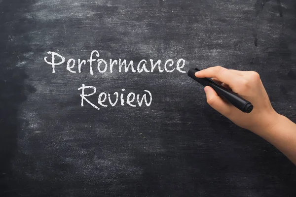 Woman hand points to words Performance Review written on black chalkboard. Labor productivity and efficiency concept. Employee evaluation