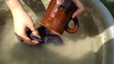 Person hands wash old handmade clay mug. Gardener with tattoos on wrist takes blue cloth to wipe mug in bowl of water at sunlight closeup