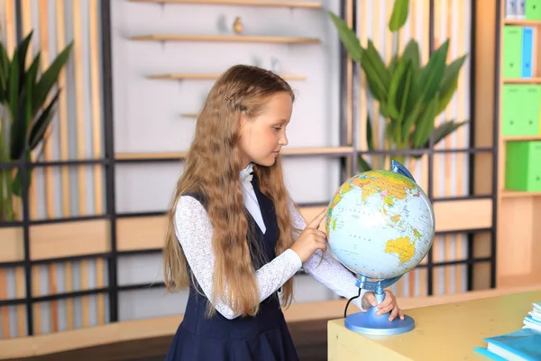 Retrato de uma menina de uniforme escolar com um globo nas mãos. — Fotografia de Stock