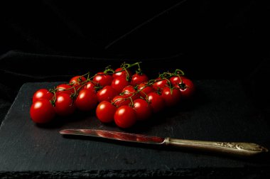 Siyah arka planda olgun kırmızı kiraz domatesleri. Bir sürü küçük kırmızı domates ve siyah tahta üzerinde eski bir bıçak..