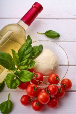 Şarap şişesi, kiraz domatesleri, fesleğen, mozzarella beyaz ahşap bir masada..