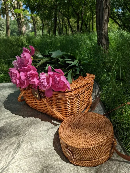 Wooden basket and bag with flowers on summer picnic with green g