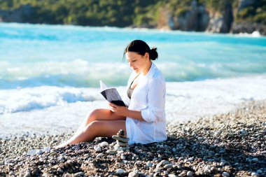 Bir kız deniz kenarında oturur ve kitap okur..
