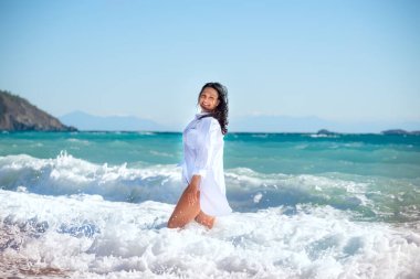 Dalgaların köpüğünde beyaz gömlekli ıslak saçlı bir kız denizin gök mavisi dalgalarının arka planında..