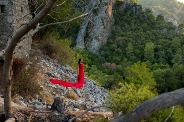 Kırmızı elbiseli bir kız, bir kayanın üstünde kırmızı elbiseli bir kızın kalıntılarında rüzgarda sallanıyor dağlarda kayalar ve engeller arasında. Olimpos Dağı. Türkiye. 