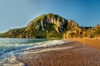 Dağ yamaçlarında antik bir kalenin kalıntılarıyla sahil ve dağların manzarası. Hindi. Kemer. Cirali. Olimpiyat Dağı, Tahtali.