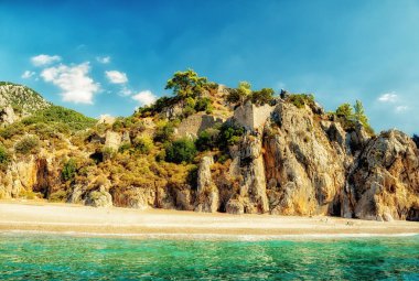 Dağ yamaçlarında antik bir kalenin kalıntılarıyla sahil ve dağların manzarası. Hindi. Kemer. Cirali. Olimpiyat Dağı, Tahtali.