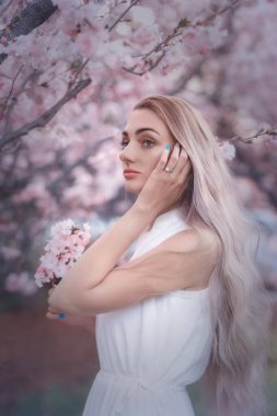 Bahar bahçesinde pembe sakuralı uzun saçlı hassas bir kız. Yüzünde seçici odaklanma olan sanatsal bir fotoğraf..
