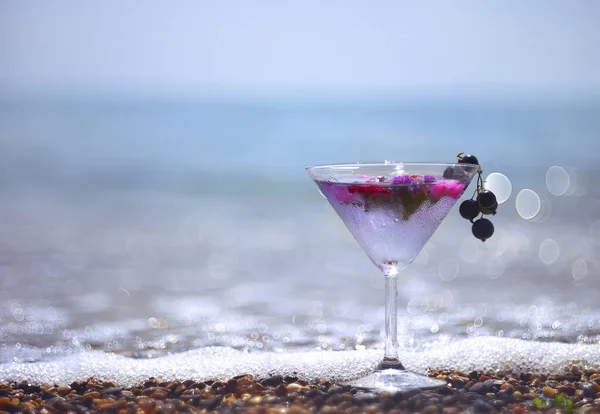 Cooling original drink with ice cubes and flowers on the beach on the sand with a sea view.