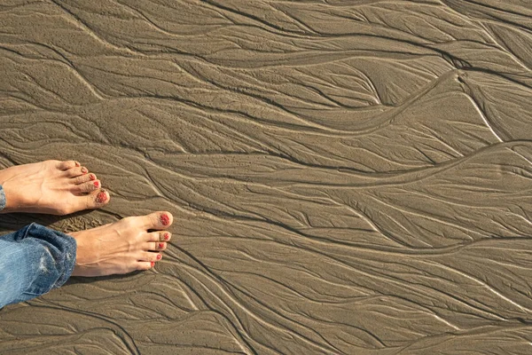 Bare feet in the sand on the beach sand. Patterns on the sand from the water at low tide.