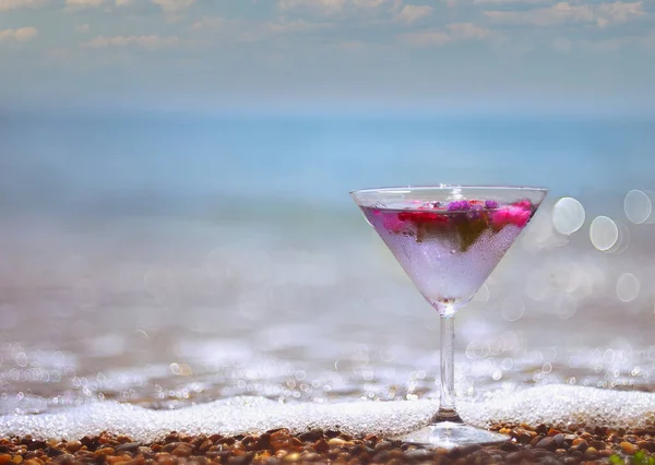 Cooling original drink with ice cubes and flowers on the beach on the sand with a sea view.