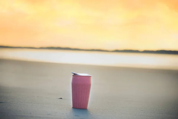 A cup of thermos with coffee on the sand of a deserted beach of the ocean coast in the early morning