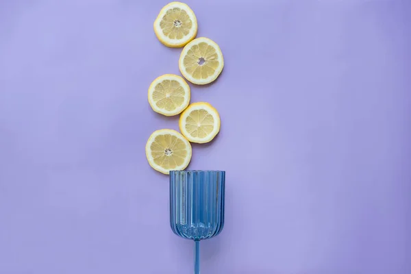 A glass and slices of lemon on a lilac background. View from above