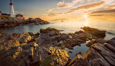  Lighthouse on the beach at dawn. panoramic photo.A beautiful coastline covered with stones, the sun's rays illuminating everything around in the early morning. USA. Portland. Maine. 
