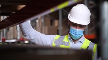 Kasklı maskeli adam depoda envanter çıkarıyor.