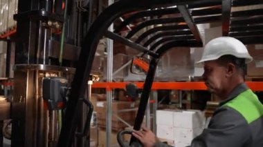 Sert şapkalı depo çalışanı forklift kullanıyor.