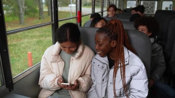 Chicas alegres multirraciales usando el teléfono en el autobús escolar — Vídeo de stock