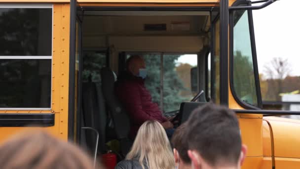 Μασκοφόροι διαφορετικοί μαθητές που εισέρχονται κίτρινο σχολικό λεωφορείο — Αρχείο Βίντεο