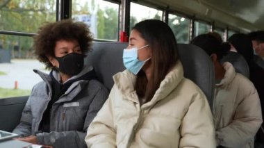 Okul otobüsünde iletişim kuran maskeli öğrenciler.
