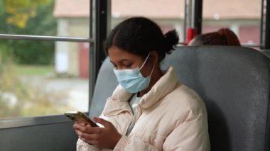 Okul otobüsünde telefon kullanan maskeli ırk kızı.