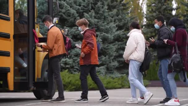 Занят на телефонах подростки садятся в школьный автобус — стоковое видео