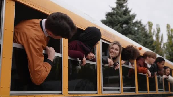 Adolescenti gioiosi con teste fuori dai finestrini dello scuolabus — Video Stock