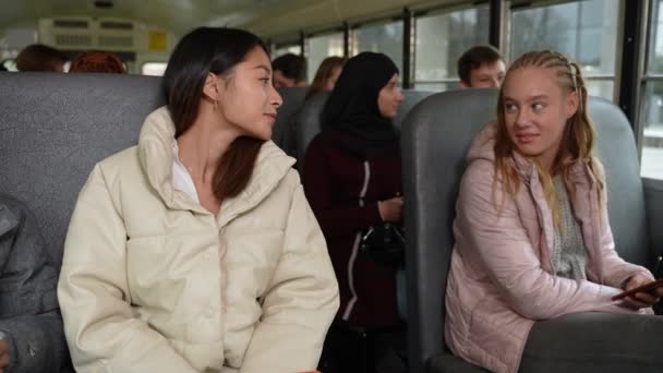 Wesołe wielorasowe dziewczyny rozmawiające w autobusie szkolnym — Wideo stockowe