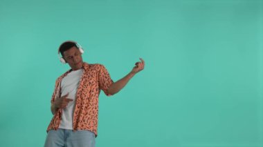 Pozitif Afro-Amerikalı adam kulaklıkla rock müzik dinliyor ve dans sırasında bas gitar çalıyormuş gibi yapıyor. Neşeli koyu tenli adam mavi arka planda dans ve müzikten zevk alıyor.