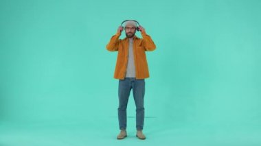 Gözlüklü neşeli sakallı erkek kulaklık takıyor ve rock müzik dinlerken hayali bas gitar çalıyor. Neşeli adam mavi arka planda izole müzik ritmine geçmekten hoşlanıyor.