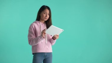 Tabletle düşünen düşünceli genç bir kadın. Doğru kararla gülümseyen ve fikir uçup gittiğinde kaşlarını çatan. Arka planda izole edilmiş bir projede çalışan düşünceli Asyalı kızın portresi