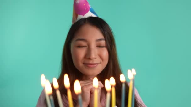 生日女孩戴着节日圆锥帽的特写 吹灭蓝色背景下的蜡烛 快乐的亚洲女人在庆祝生日 感到快乐 — 图库视频影像