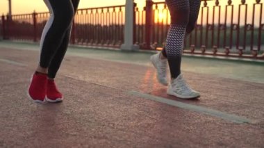 Akşamki kardiyo egzersizi sırasında spor ayakkabılı kadın ayaklarının yaya köprüsünden geçişi. Spor kıyafetleri içinde spor yapan iki sağlıklı kadın, aktif sağlıklı hobi, kentsel aktivite konsepti.