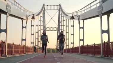 Aktif sabah antrenmanı sırasında başörtüsü ve spor giysisi giyen müslüman kadın koşucular. Fit Arap kadınları şehir köprüsünde hızlı koşuyor, sağlıklı spor yaşam tarzı konsepti