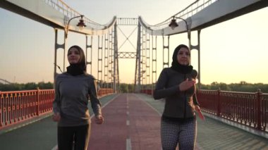 Aktif Müslüman koşucular sabah antrenmanlarında spor kıyafetleri ve başörtüsü giyerek yarışacaklar. Sportif Arap atletler şehir köprüsünde hızlı koşuyorlar, spor yaşam tarzı konsepti