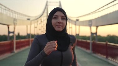 Aktif spor müslim kadın tesettür giymiş sabahları koşu yaparken yakın çekim. Yetişkin fit bir kadın dışarıda spor yapıyor, şehir köprüsünde koşuyor, sağlıklı hobi, aktif yaşam tarzı konsepti.