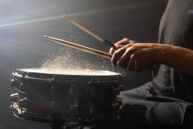 Davul sopaları trampet davuluna çarpıyor sahne ışıklarının altında siyah arkaplanda su sıçrıyor..
