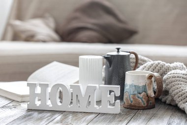 Dekoratif sözcük ev, çay, örgü ögesi ve odanın arka planındaki bulanık dekorasyon detaylarıyla ev kompozisyonu.