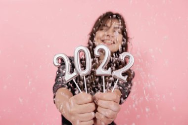 Pembe arka plandaki neşeli kız gülümsüyor ve 2022 rakamlarını elinde tutuyor, yeni yılı kutluyor..