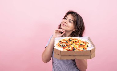 Pembe arka planda bir kutu pizzayla tatminkar bir kız, fotokopi alanı..