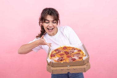 Güzel esmer kız gülümsüyor, elinde teslimat için bir kutu pizza tutuyor, pembe arka plan, fotokopi alanı.