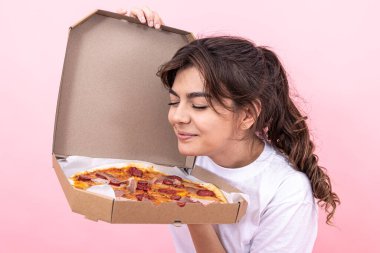 Tatlı esmer kız açık bir teslimat kutusundan pizza kokluyor, pembe arka plan..
