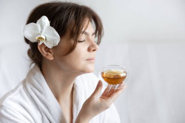 Saçında orkide çiçeği olan beyaz cüppeli genç bir kadın çayın, spa tedavisinin ve rahatlamanın tadını çıkarıyor..