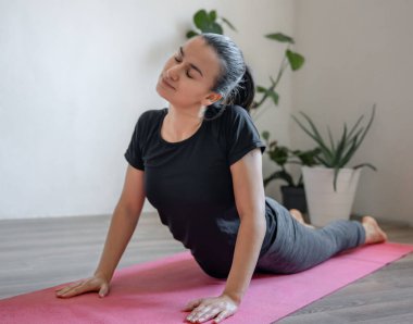 Genç bir kadın paspasın üzerinde asanas antrenmanı yapıyor, evde yoga yapıyor, vücudun kaslarını esnetiyor..