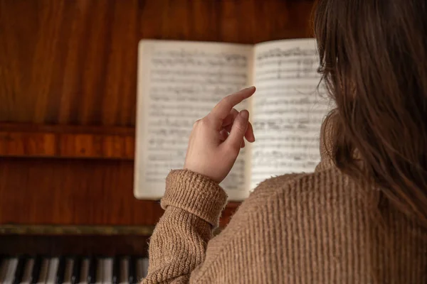 Mano femenina sobre un fondo borroso de notas musicales en el piano. — Foto de Stock