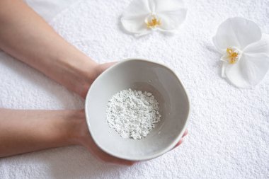 Kadının elinde kozmetik kilden bir yüz maskesi olan bir tabak var..