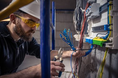 Bir erkek elektrikçi elektrik kablosuyla santralde çalışıyor..