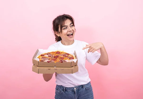 Menina atraente alegre com pizza em uma caixa em um fundo rosa. — Fotografia de Stock