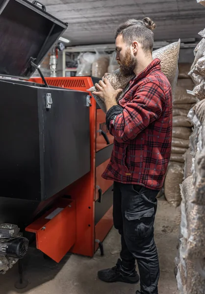 El hombre carga los pellets en la caldera de combustible sólido, trabajando con biocombustibles. — Foto de Stock