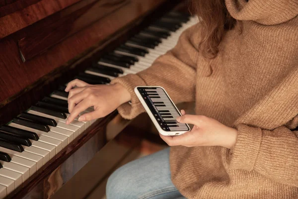 Женщина учится играть на пианино с помощью приложения на телефоне. — стоковое фото